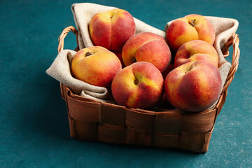 Wicker basket with sweet peaches on blue table
