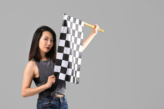 Beautiful Asian woman with racing flag on grey background