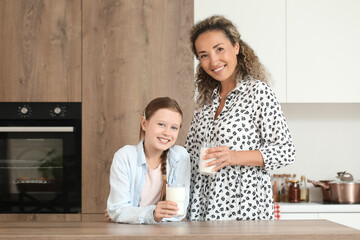 Happy mother with her little daughter drinking milk in kitchen