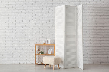 Folding screen with shelving unit and ottoman near white brick wall