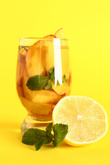 Glass of fresh peach lemonade with mint on yellow background