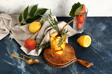 Wooden board with glass of fresh peach lemonade and rosemary on blue table