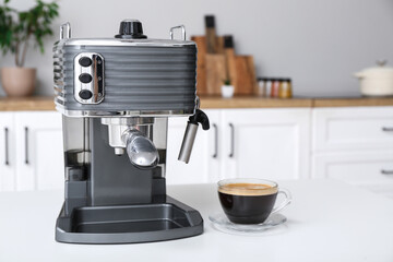 Modern coffee machine with glass cup of hot espresso on table in kitchen