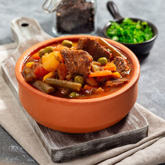 Vegetable beef stew with potato, green beans, carrot, peas and corn, in ceramic bowl, square format