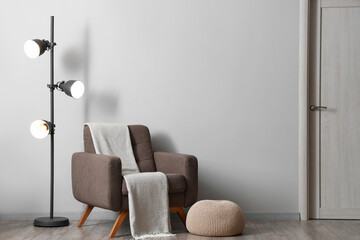Interior of living room with soft armchair, pouf and glowing lamp