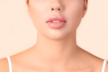 Obraz na płótnie Canvas Young woman with beautiful lips on beige background, closeup