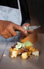 Unrecognizable woman holding knife in her hand and cutting vegetables while cooking vegetable salad near kitchen table, close up