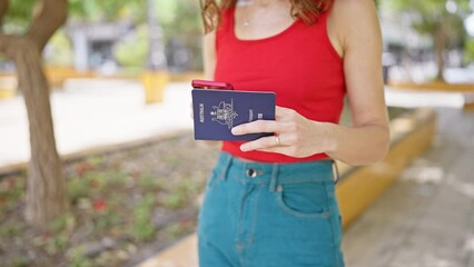 Young woman using smartphone holding united states passport at park