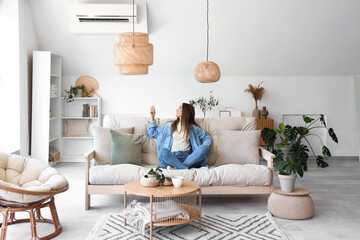 Young woman switching on air conditioner in living room