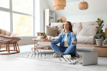 Young woman with headphones meditating on carpet in living room - Powered by Adobe