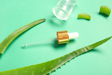 Glass bottle with aloe vera essential oil on green background, closeup