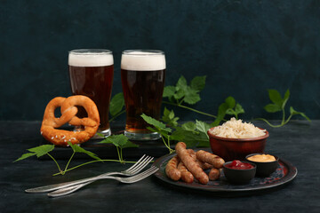 Glasses of cold beer with Bavarian sausages, sauces and sauerkraut on dark grunge background....