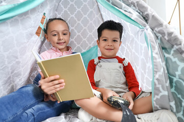 Cute little children reading adventure book in play tent at home