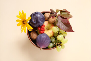 Bowl with different fresh fruits on beige background