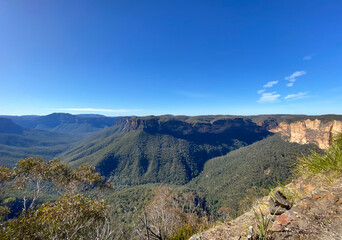 Fototapeta na wymiar Spectacular views from a mountain-top lookout. Green mountains in the horizon. Blue mountains, Australia, NSW. Unusual rock formation. Summit of the mountain.