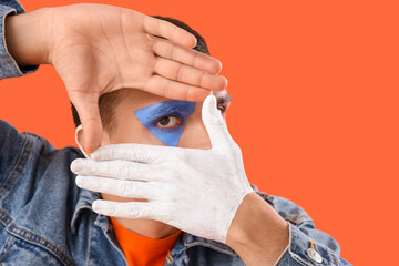 Young man with painted body making frame gesture on orange background, closeup