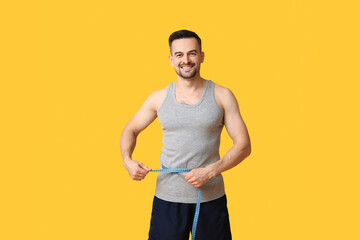 Fototapeta na wymiar Handsome sporty young man measuring his waist on yellow background. Weight loss concept