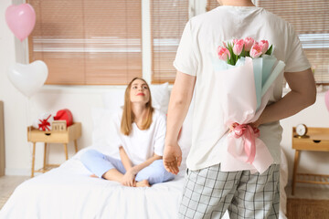 Young man greeting his girlfriend with bouquet of tulips for Valentine's Day at home
