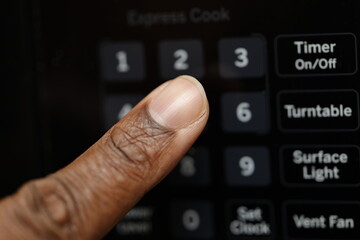 A close-up of a finger pressing the number '1' on a microwave keypad