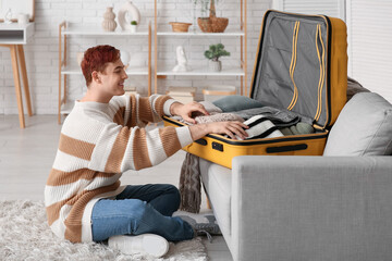 Young man packing clothes in suitcase at home
