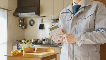 リビング・キッチンで電卓を持つ作業服の男性　見積りイメージ