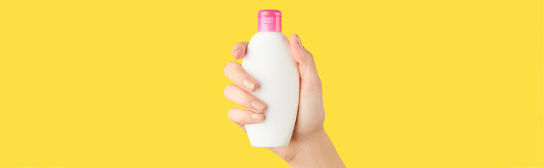 Womans hand holding white bottle on yellow background. Self care concept.