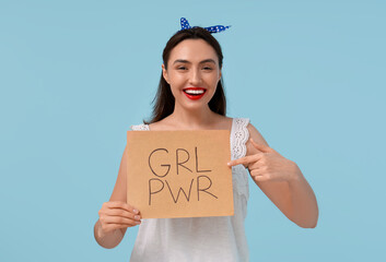 Beautiful young pin-up woman holding paper with text GRL PWR on light blue background