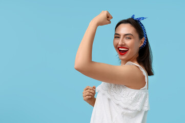 Beautiful happy pin-up woman showing her muscles on light blue background