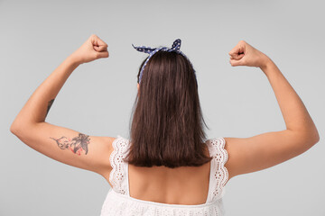 Beautiful pin-up woman showing her muscles on light background, back view