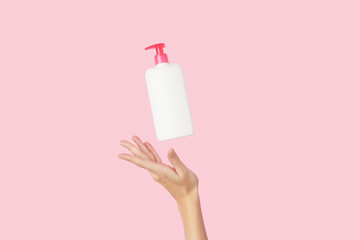 Womans hand holding white bottle on pastel pink background
