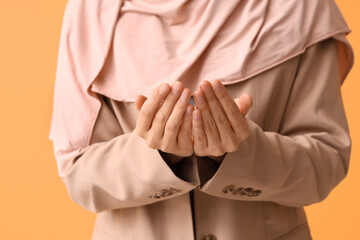 Young Muslim woman praying on yellow background, closeup
