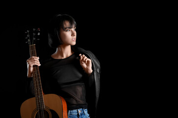 Fototapeta na wymiar Cool young woman with guitar on black background