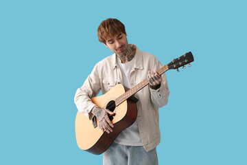 Obraz premium Cool tattooed young man playing guitar on blue background