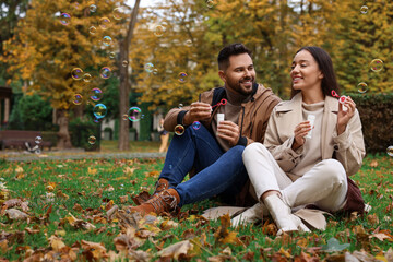 Fototapeta premium Happy young couple blowing soap bubbles in autumn park, space for text