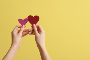 Female hands with paper hearts on yellow background. Valentine's Day celebration