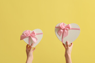 Female hands with gift boxes in shape of heart on yellow background. Valentine's Day celebration