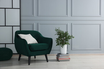 Stylish armchair with pillow and houseplant on floor near light grey wall indoors, space for text. Interior design