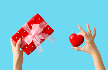 Female hands with gift box and heart on blue background. Valentine's Day celebration