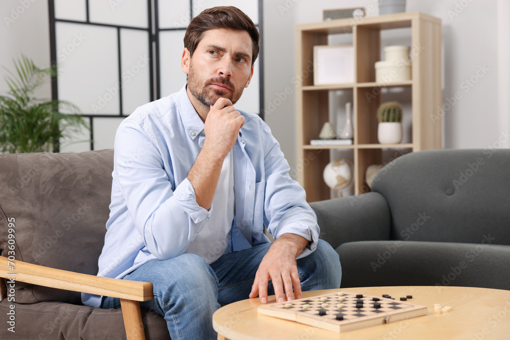 Poster Thoughtful man playing checkers in armchair at home