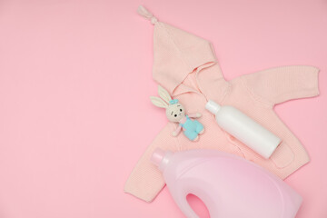 Bottles of laundry detergents, baby sweatshirt and toy bunny on pink background, flat lay. Space for text