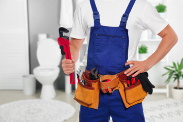 Plumber with pipe wrench and tool belt in bathroom, closeup. Space for text