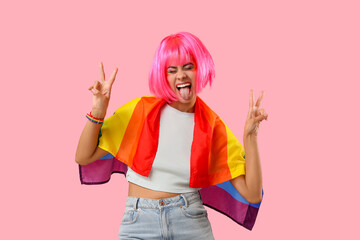 Funny African-American woman with rainbow flag showing victory gesture on pink background. LGBT...