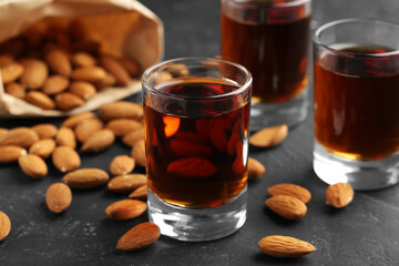 Glasses with tasty amaretto liqueur and almonds on dark gray table, closeup