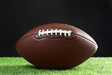 Leather American football ball on green grass against black background, closeup