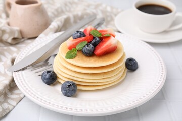 Delicious pancakes with strawberries, blueberries and mint on white tiled table, closeup