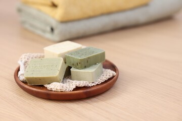 Tray with soap bars on light wooden table, space for text. Spa therapy