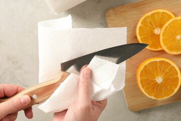 Woman wiping knife with paper towel at table, top view