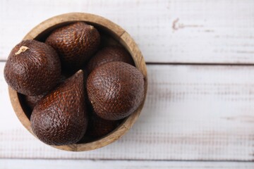 Fresh salak fruits in bowl on white wooden table, top view. Space for text