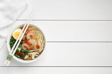 Tasty ramen with shrimps in bowl and chopsticks on white wooden table, top view. Space for text