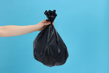 Woman holding plastic bag full of garbage on light blue background, closeup. Space for text